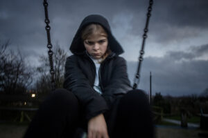 Student sitting on swing in a coat looking sad